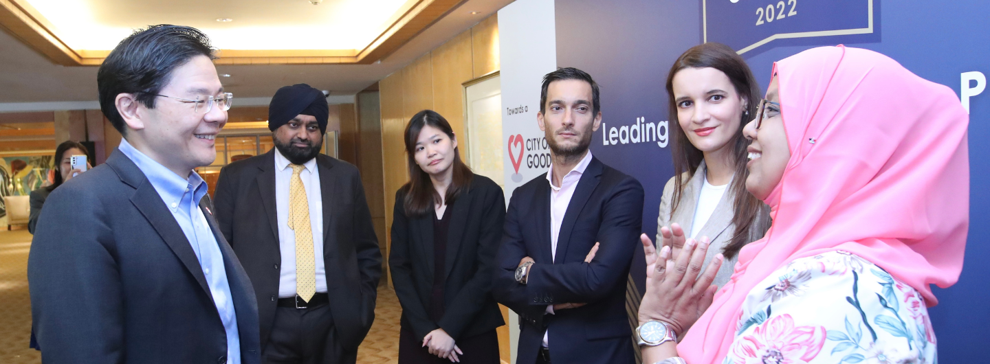Group of people in business attire stand near "City of Good" sign at event.